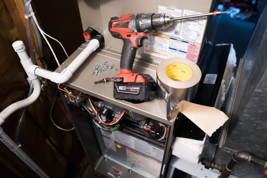 Drill, screws and foil tape on top of a furnace during a repair